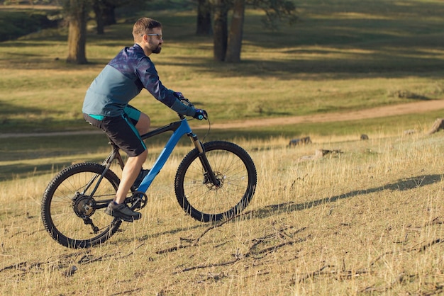 Pokonywanie górskich szczytów przez rowerzystę w krótkich spodenkach i koszulce na nowoczesnym rowerze hardtail z włókna węglowego z widelcem z amortyzacją pneumatyczną