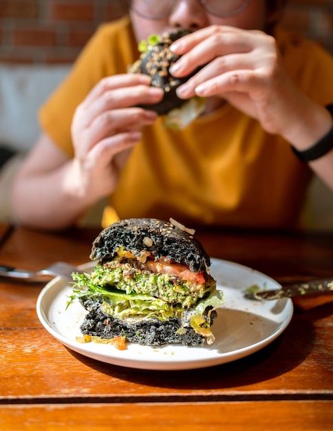 Pokrój połowę burgera z węglem brokułowym z komosy ryżowej, polane guacamole, salsą mango i świeżą sałatką, podane na białym talerzu. Kreatywny wegański posiłek dla wegetarian.