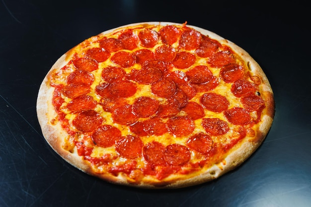 Pokrojona pizza z kiełbasianym sosem pomidorowym, mozzarellą, cebulą i brzegiem ciasta zwieńczona twarogiem na czarnym tle