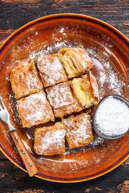 Pokrojone greckie ciasto Bougatsa z ciastem filo i kremem z kaszy manny. Ciemne drewniane tło. Widok z góry.