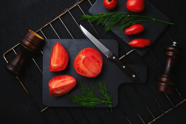 Pokrojone pomidory łupek koperek zielony dwa młynki do przypraw i nóż z drewnianą rączką na grillu