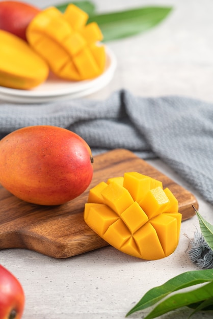 Pokrojone w kostkę świeże owoce mango na białym talerzu nad drewnianą deską do krojenia z liśćmi na szarym tle stołu