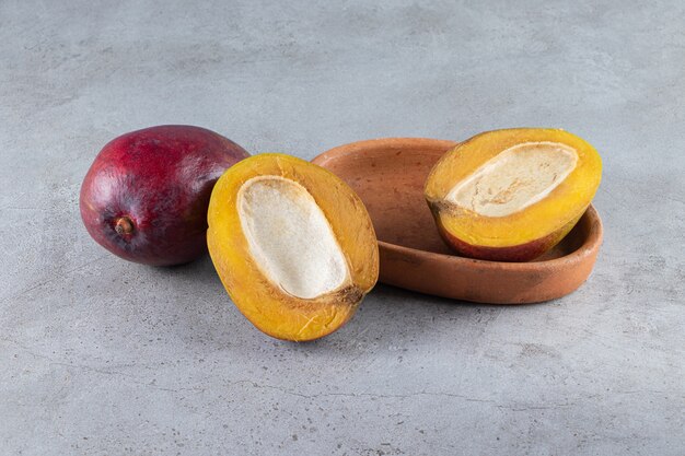 Pokrojone w plastry i całe świeże dojrzałe owoce mango umieszczone na kamiennym stole.