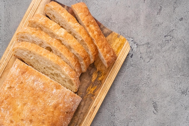 Pokrojony bochenek świeżo upieczonego chleba ciabatta na szarym stole.