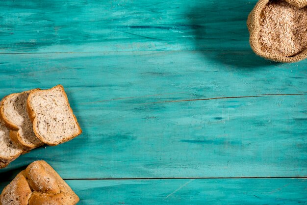 Pokrojony cały chleb i małą torbę z mąki pełnoziarnistej na teksturowanej niebieskiej przestrzeni drewna na tekst, widok z góry.