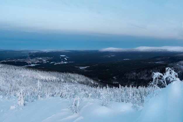 Pokryte śniegiem zbocze wzgórza polarnego zimą wczesnym rankiem z dalekim widokiem na Kandalaksha, miasto portowe w północnej Rosji. Zimowy krajobraz polaris. Mroźna zima.