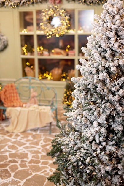 Pokryty śniegiem dom jest udekorowany na nowy rok. Zimowy dziedziniec w stylu vintage, ozdobiony sylwestrowymi dekoracjami, choinkami, lampionami i przytulną ławką. Miękka selektywna ostrość.