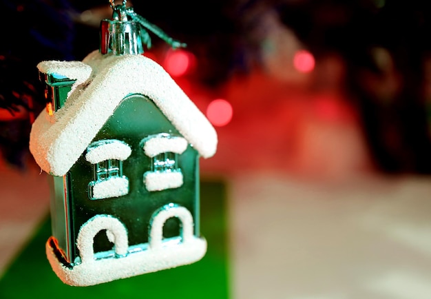 Pokryty śniegiem zielony mały ornament domowy z czerwonym świątecznym dekorowaniem światła Bokeh w tle