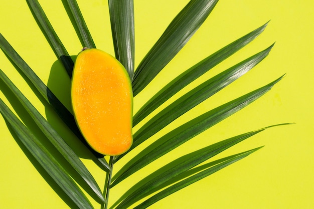 Pół pokrojone dojrzałe mango na liściach tropikalnej palmy na zielonej powierzchni