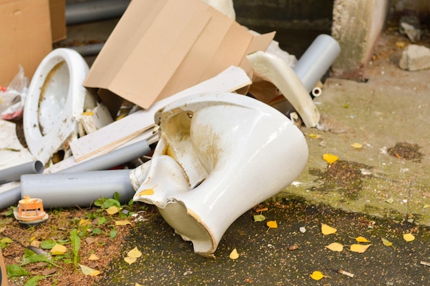 Połamane, porzucone białe ceramiczne muszle klozetowe leżą wśród śmieci na szarej ziemi na ulicy