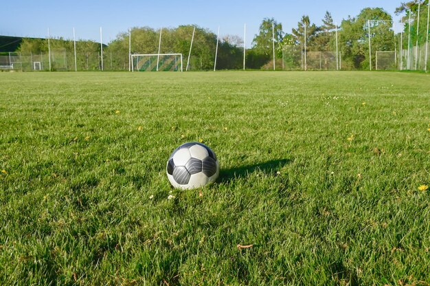 Zdjęcie pole piłkarskie z bramką w tle i piłką piłkarską na pierwszym planie mnóstwo miejsca do kopiowania