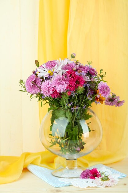 Polne kwiaty w szklanym wazonie na stole na żółtym tle tkaniny