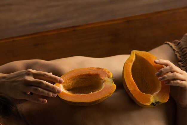 Połowa owoców papai na plecach kobiety. Pachnąca pulpa z owoców tropikalnych. Słodka świeża papaw, surowe wegańskie jedzenie