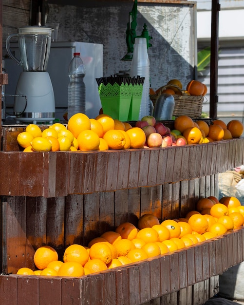 Pomarańcze i jabłka leżą na drewnianych półkach i koszach w ulicznym sklepie z sokami i koktajlami
