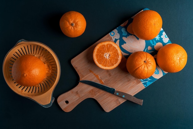 Pomarańcze na desce kuchennej i sokowirówka na ciemnym tle