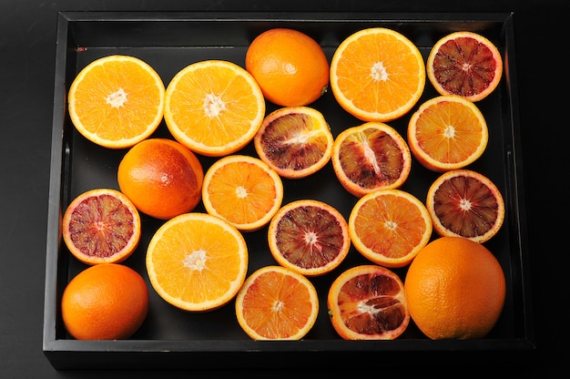 Pomarańcze w całości i pokrojone na pół na czarnej tacy