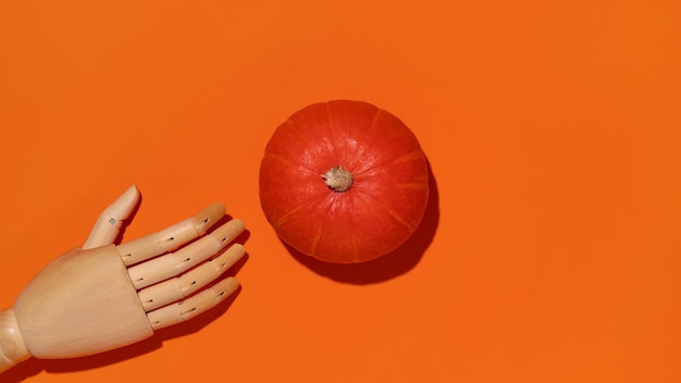 Pomarańczowa dynia i drewniana ręka na pomarańczowym tle