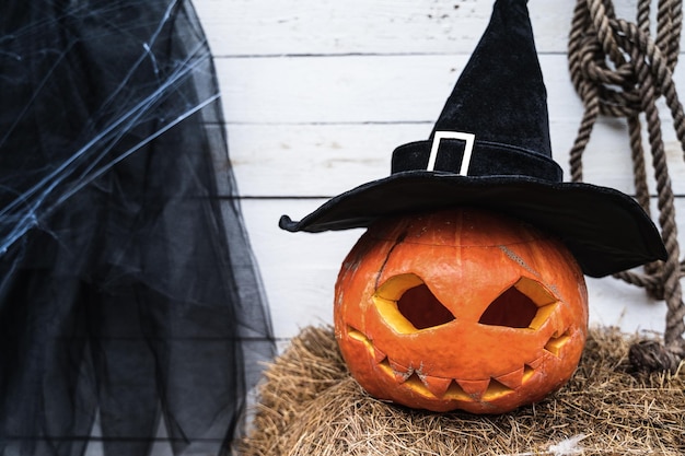 Pomarańczowa dynia na halloween w czarnym kapeluszu czarownicy jackolantern z przerażającymi rzeźbionymi oczami usta Stóg siana w pobliżu stodoły DIY domowa dekoracja uliczna rozrywka dla dzieci horror