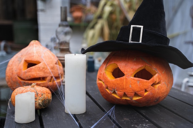 Pomarańczowa dynia na halloween w czarnym kapeluszu czarownicy jackolantern z przerażającymi rzeźbionymi oczami ustaŚwiece na drewnianym stole w pobliżu stodoły DIY homestreet dekoracja rozrywka dla dzieci horror