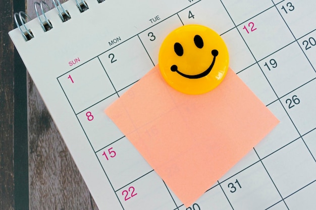 Zdjęcie pomarańczowa papierowa notatka z uśmiechniętą twarzą i przyklejona do tła kalendarza