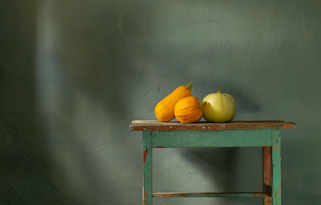 Pomarańczowe dynie na starym drewnianym stole na tle zielonej ścianie