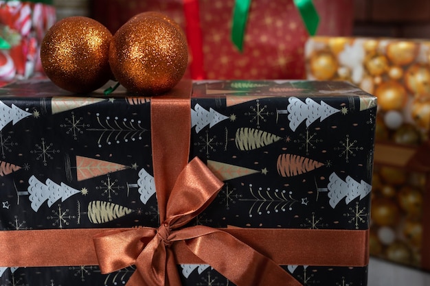 Pomarańczowe kulki bożonarodzeniowe leżą obok pudełka z prezentami związane dużym łukiem