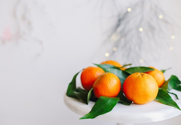 Pomarańczowe mandarynki na szarym tle w noworocznym wystroju z brązowymi szyszkami i zielonymi liśćmi. Dekorację świąteczną z mandarynkami. Pyszna słodka klementynka.