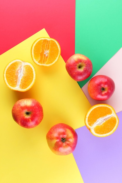 Pomarańczowe owoce i czerwone jabłka na wielokolorowym tle Połówki pomarańczy i jabłek na kolorowym papierze Kopiowanie miejsca