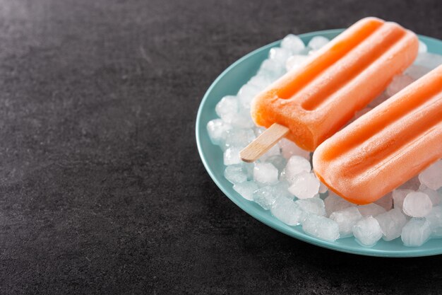 Pomarańczowe popsicles na niebieskim talerzu na czarnym tle