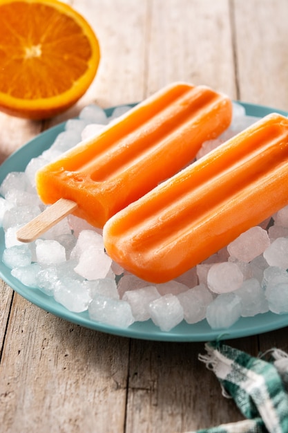 Pomarańczowe popsicles na niebieskim talerzu na drewnianym stole