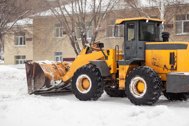 Pomarańczowy ciągnik czyści śnieg z drogi i ładuje go do ciężarówki Czyszczenie dróg w mieście