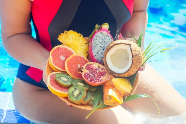 Pomarańczowy kokosowy granat smoczy ananas na talerzu w rękach kobiety w stroju kąpielowym na tle detoksykacji basenowej