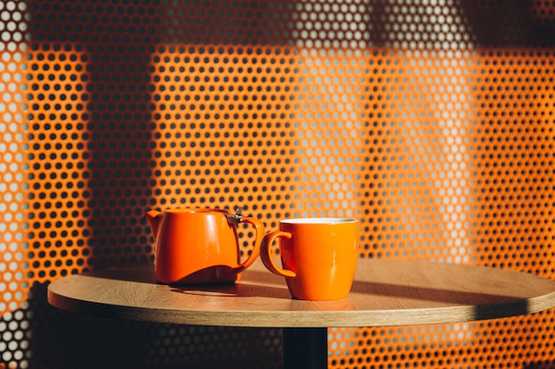 Pomarańczowy kubek i czajnik na stole we wnętrzu eleganckiej kawiarni
