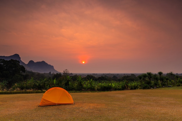 Pomarańczowy namiot wycieczkowicza na trawniku rano.