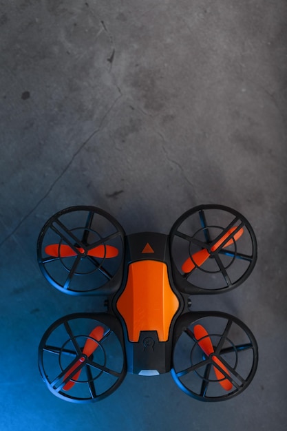 Zdjęcie pomarańczowy quadcopter mini dron szpiegowski na ciemnym tle z niebieskim podświetleniem