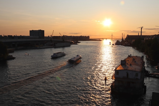 Pomarańczowy zachód słońca nad rzeką z dużym mostem i łodziami