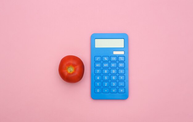 Pomidor i kalkulator na różowym tle pastel. Płaska kompozycja świecka.