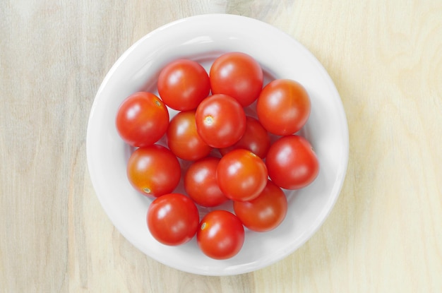 Pomidory czereśniowe w białym talerzu na drewnianym tle widok z góry