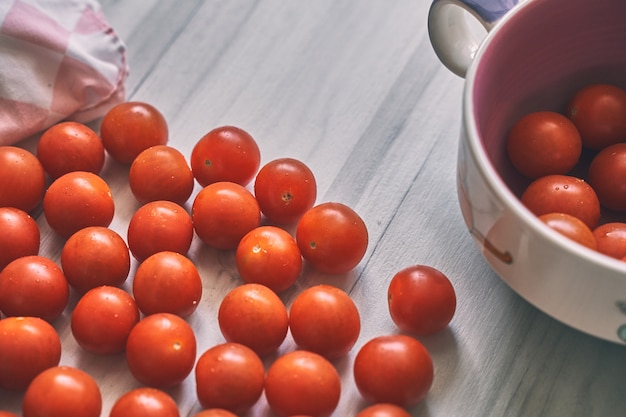 Pomidory czereśniowe w fioletowej misce obok jasnej serwetki w kratkę