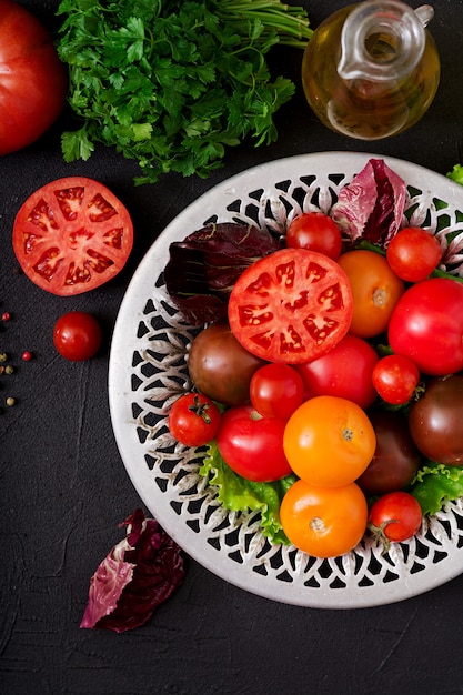 Pomidory w różnych kolorach z zielonymi ziołami w misce na czarnym stole