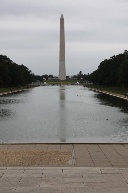 Pomnik Waszyngtonu przez odbijający się basen na tle nieba