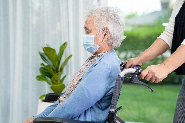 Zdjęcie pomóż azjatyckiej starszej lub starszej starszej kobiecie siedzącej na wózku inwalidzkim i noszącej maskę do twarzy w celu ochrony przed infekcją covid-19 coronavirus