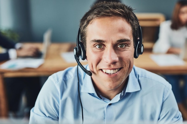 Pomoże ci przez telefon Portret skoncentrowanego młodego mężczyzny rozmawiającego z klientem przez telefon podczas używania zestawu słuchawkowego w biurze w ciągu dnia