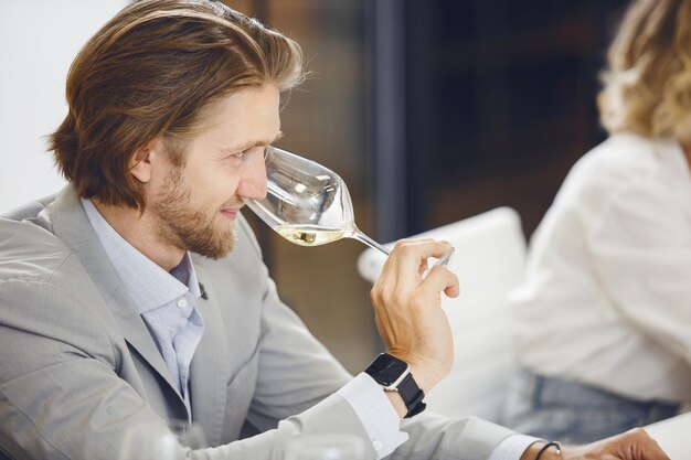 Zdjęcie pomyślnie wyglądający mężczyzna wąchający i degustujący białe wino w szklance oceniający jego właściwości smak