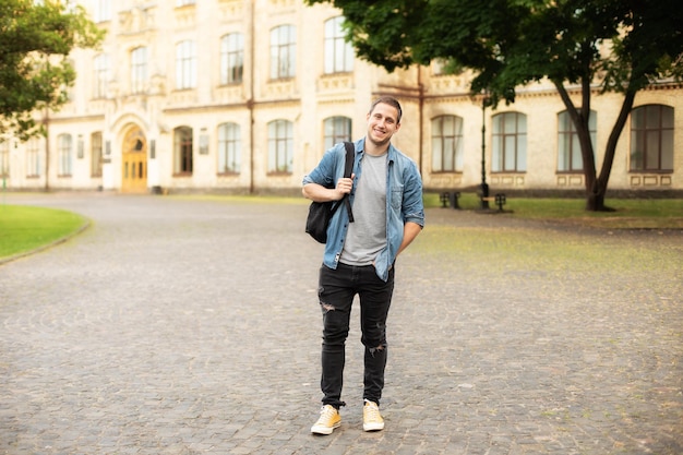 Pomyślny student mężczyzna stoi z plecakiem za parkiem w pobliżu kampusu.