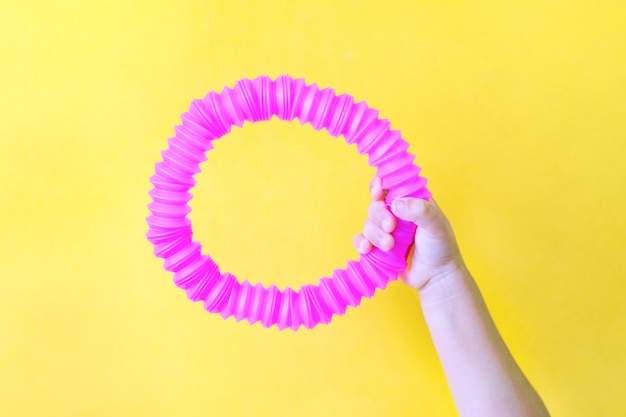 Zdjęcie pop rura. antystresowa sensoryczna plastikowa zabawka z tuby pop w rękach dziecięcego trendu z 2021 roku. żółte tło