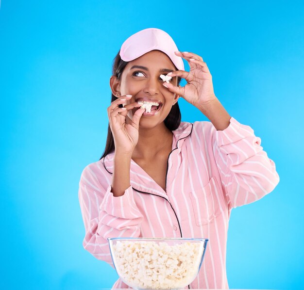 Zdjęcie popcorn piżama i zabawne z kobietą na niebieskim tle w studiu oglądając film dla rozrywki zabawne wideo i noc z atrakcyjną młodą kobietą jedzącą przekąskę podczas strumieniowania
