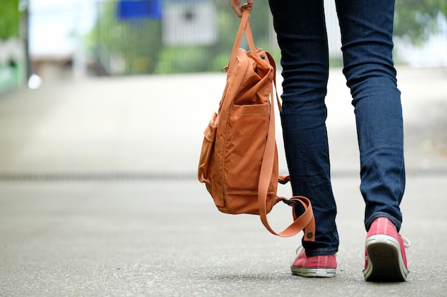 Popiera studencka dziewczyna trzyma szkolną torbę podczas gdy chodzący w szkolnym kampusu tle