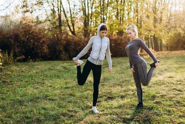 Poranna fitness w parku. Dwie młode dziewczyny robią ćwiczenia.