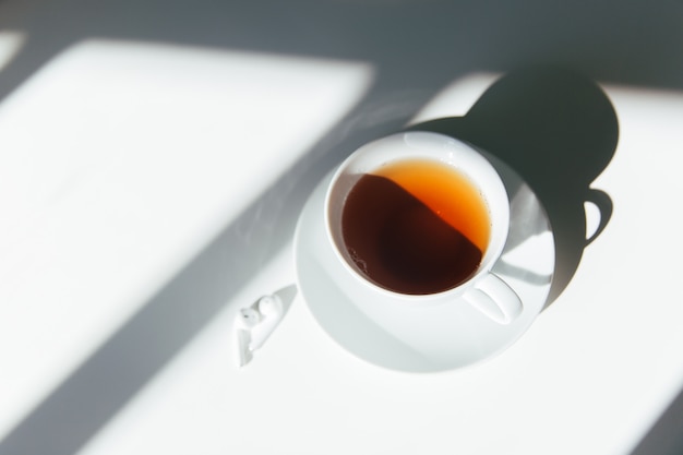Poranna herbata na białym stole z białymi słuchawkami. Czysty, cichy i spokojny poranek